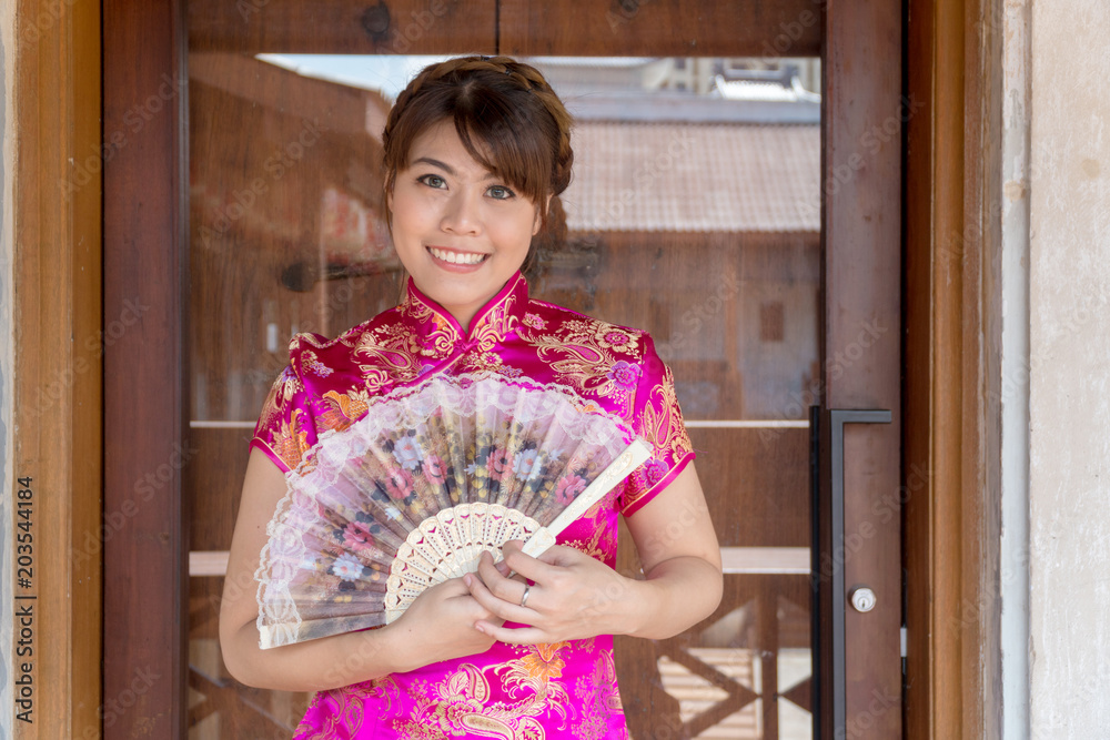 Portrait beautiful young woman wear cheongsam deep pink dress holding a fan looking at camera. Festivities and Celebration concept