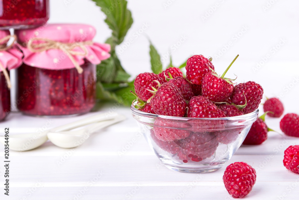 Red fresh raspberries in a glass bowl with green leaves on white background. Red fresh raspberries in a glass bowl with green leaves on white background.