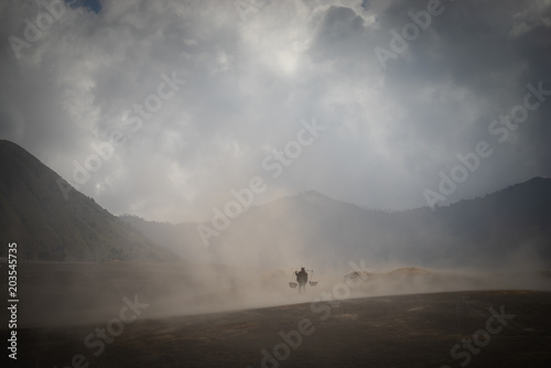Fototapeta Naklejka Na Ścianę i Meble -  BROMO, INDONESIA - 16th APRIL 2018; Unidentified local people of Tengger walking in sandstorm  at savanna of Tengger caldera, Mt. Bromo, East Java of Indonesia.