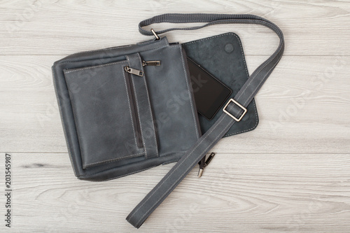 Leather shoulder bag for men with mobile phone on it with grey wooden background