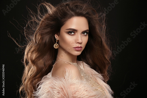 Brunette in fashion fur coat. Beauty portrait of gorgeous sexy brunette woman with long healthy hair and evening makeup isolated on black background. Fashionable girl portrait. Vogue style.