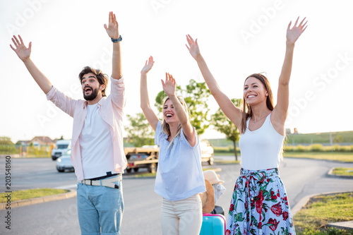 Group of friends hitchhiking on a side of the road. Jumping and waving to grab attention.