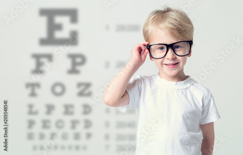 Little boy in glasses having eye test, over eye chart. Tables vision testing. Visiting a doctor pediatric ophthalmologist.