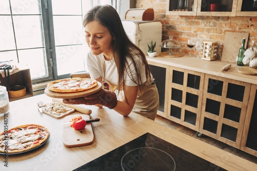 Young woman housewife baking pizza for her family at kitchen. Cooking with love, homemade recipe, culinary, food preparing concept