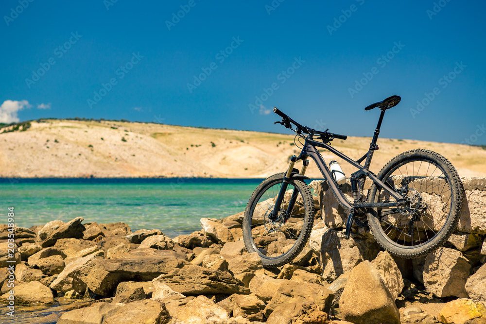 Fototapeta premium Mountain bike over sea, mountains and blue sky on a rocky beach