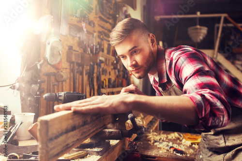 profession, carpentry, woodwork and people concept - carpenter testing wood plank evenness at workshop photo