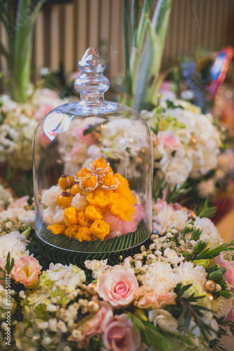 Met khanun, Thong yip and Thong yot on banana leaf. Traditional Thai dessert sweet variety in transparent glass cover and flower decoration background. Set up in Thai wedding ceremony. Select focus