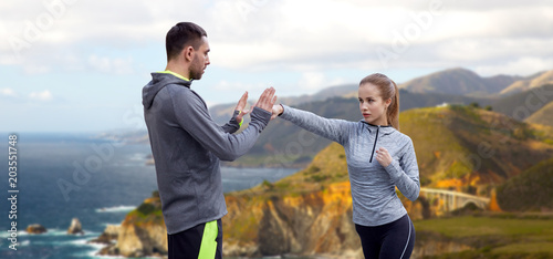 fitness, sport, martial arts and people concept - happy woman with personal trainer working on strike over bixby creek bridge on big sur coast of california background