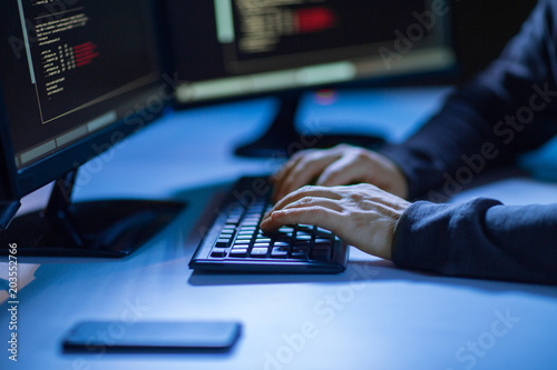 cybercrime, hacking and technology concept - hands of hacker in dark room writing code or using computer virus program for cyber attack photo