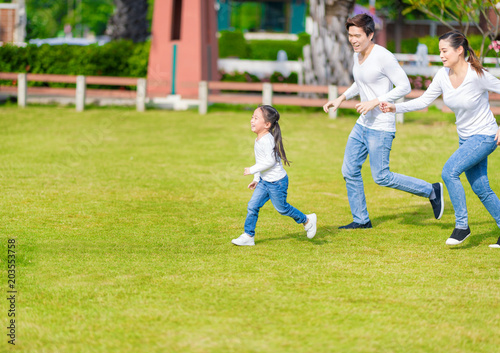 Little girl is running with parents in the park. Young family with little kid having fun in nature. © Nattanon
