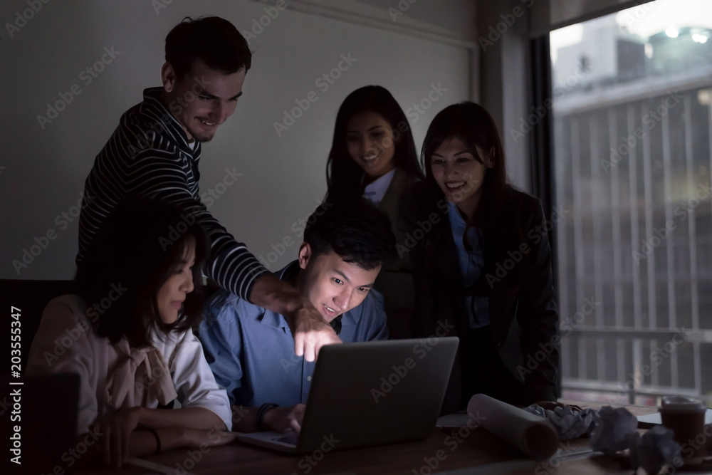 Smiling businesspeople are working with laptop  overtime late at nitgh. They are using laptop to search data. Setup studio shooting.