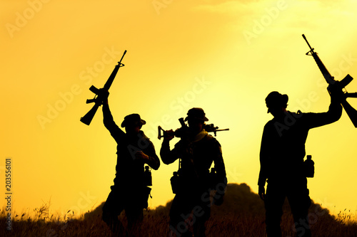 Silhouette of military soldier holding weapons overhead after get victory of war at sunset.