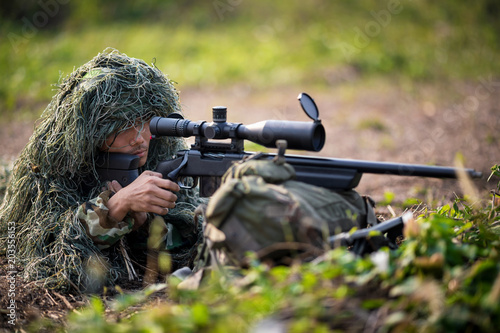 Sniper laying on the grass looking through scope at the target in deep forest.t.