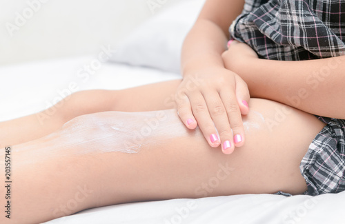 Little girl applying body lotion cream on her leg