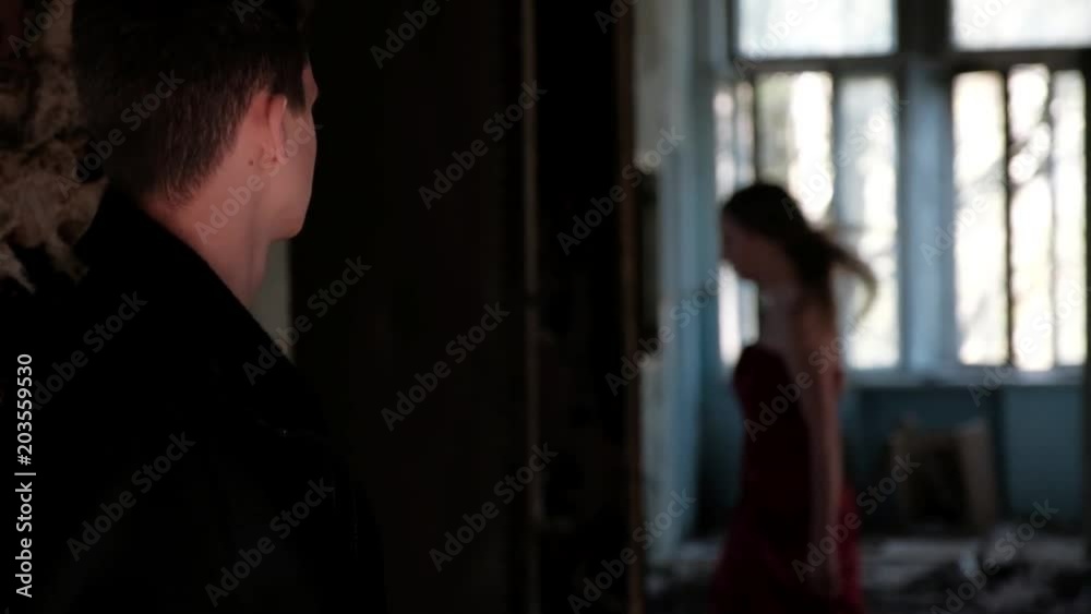 Young man comes into the room, while young beautiful woman in red long dress comes out, unwilling to see him