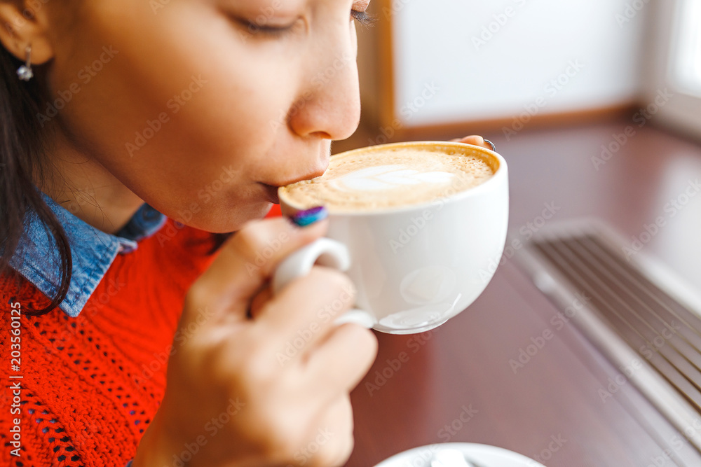 Beautiful young woman drinking coffee sitting by the window in the cafe Beautiful young woman drinking coffee sitting by the window in the cafe