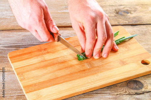 Male hands cut a green onion on a cutting board on an old wooden table.