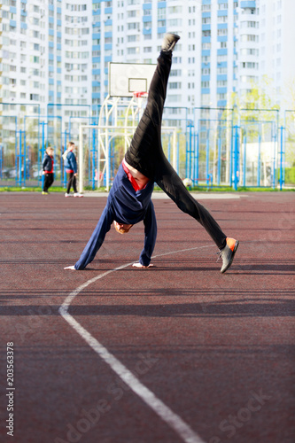 Active sporty boy in blue and black sport clothes doing a handstand on sports ground at sunset