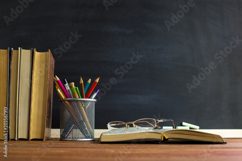 Glasses teacher books and a stand with pencils on the table, on the background of a blackboard with chalk. The concept of the teacher's day. Copy space.