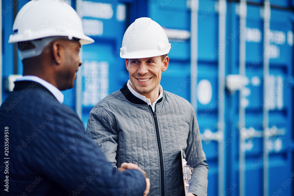 Smiling engineers shaking hands together in a shipping yard Smiling engineers shaking hands together in a shipping yard