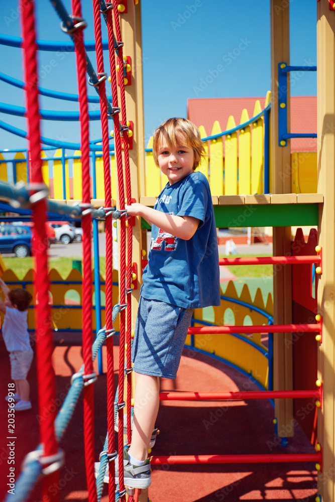 happy kid climbing the rope wall, playing games on colorful castle playground