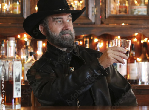 A Bearded Cowboy in Black Toasts Someone Across the Saloon