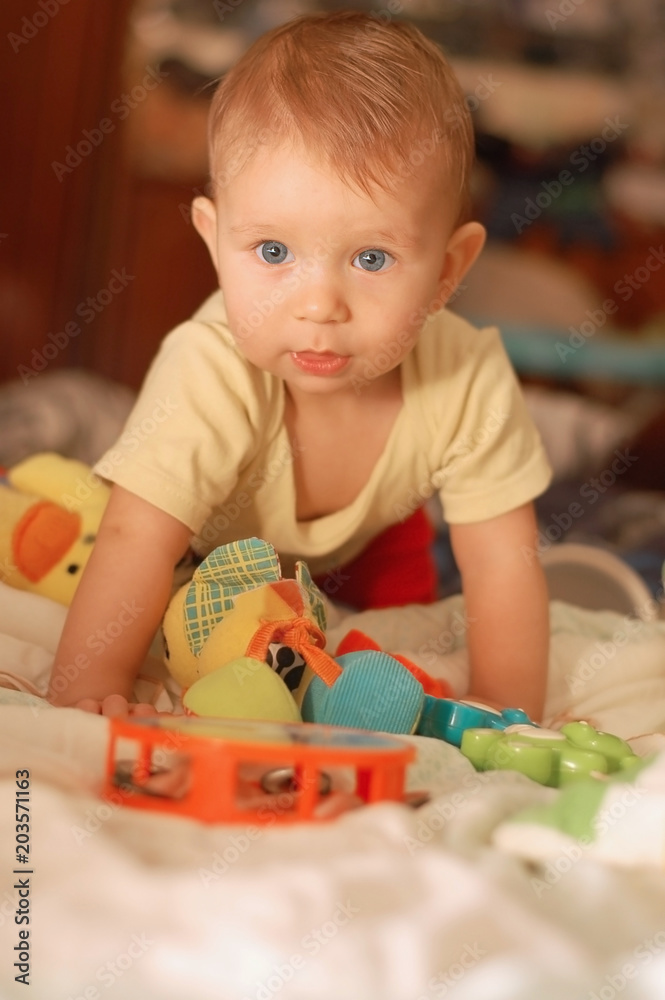 A little boy is kneeling in bed and plays with different toys. He has a beautiful enthusiastic from play face A little boy is kneeling in bed and plays with different toys. He has a beautiful enthusiastic from play face