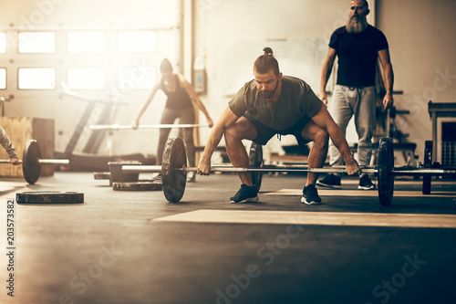Fotografie Fit young man lifting weights with others in a gym