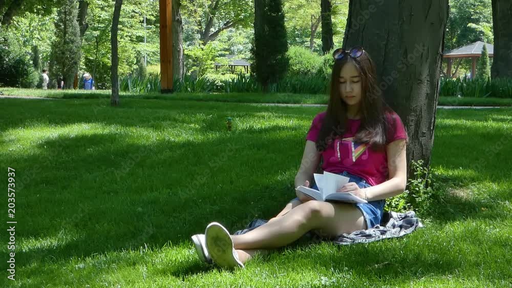 young girl reading a book in a picturesque park, sunny day. the girl of Asian appearance 