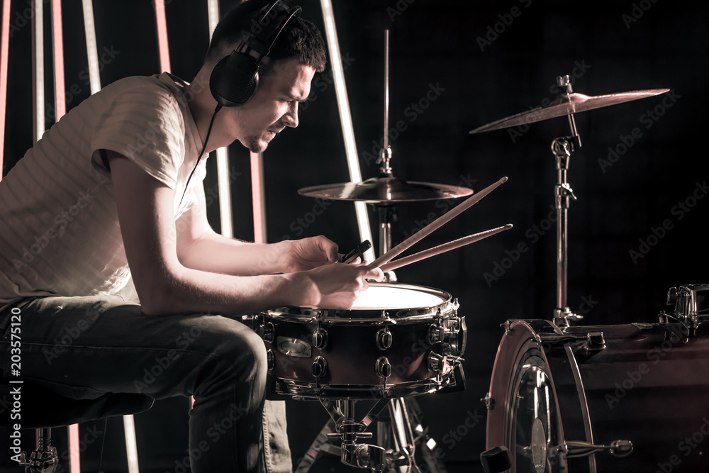 Fototapeta premium Man plays the drums in the headphones. On the background of colored lights.