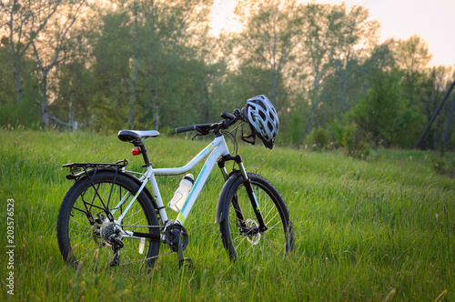 Fototapeta Naklejka Na Ścianę i Meble -  Bike with bicycle helmet on green nature background at sunset time. Countryside cycling
