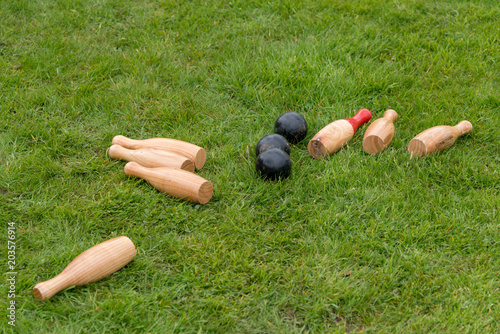 Photo set of fallen traditional wooden skittles outdoors on grass with black balls in