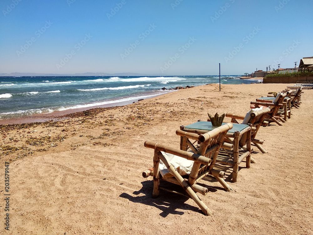 Row of bamboo chaise lounge on beach in Dahab, Sinai, Egypt. Beautiful seascape. Relax time. Row of bamboo chaise lounge on beach in Dahab, Sinai, Egypt. Beautiful seascape. Relax time.