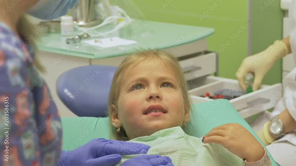 Child with a mother at a dentist's reception. The girl lies in the chair, behind her mother. The doctor works with an assistant. Procedure for drilling a tooth. Setting a temporary seal. Using the x Child with a mother at a dentist's reception. The girl lies in the chair, behind her mother. The doctor works with an assistant. Procedure for drilling a tooth. Setting a temporary seal. Using the x