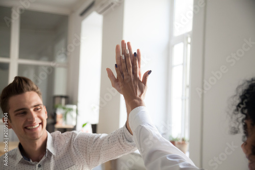 Smiling multiracial man and woman giving high five celebrating victory sharing success and good teamwork result concept, happy motivated friends, coworkers or students excited by goal achievement