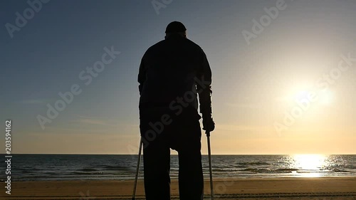 Disabled man silhouette with crutches on the beach panoramic shot
