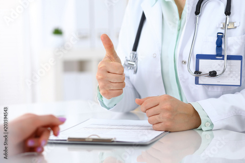 Doctor showing Ok sign and thumb up to patient while sitting at the desk in hospital office, closeup of human hands. Medicine and health care concept