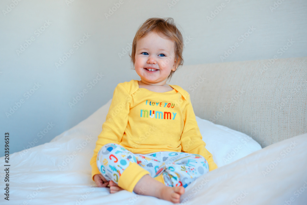 Funny little baby girl sitting in parents bed. Infant girl in yellow pajamas Funny little baby girl sitting in parents bed. Infant girl in yellow pajamas