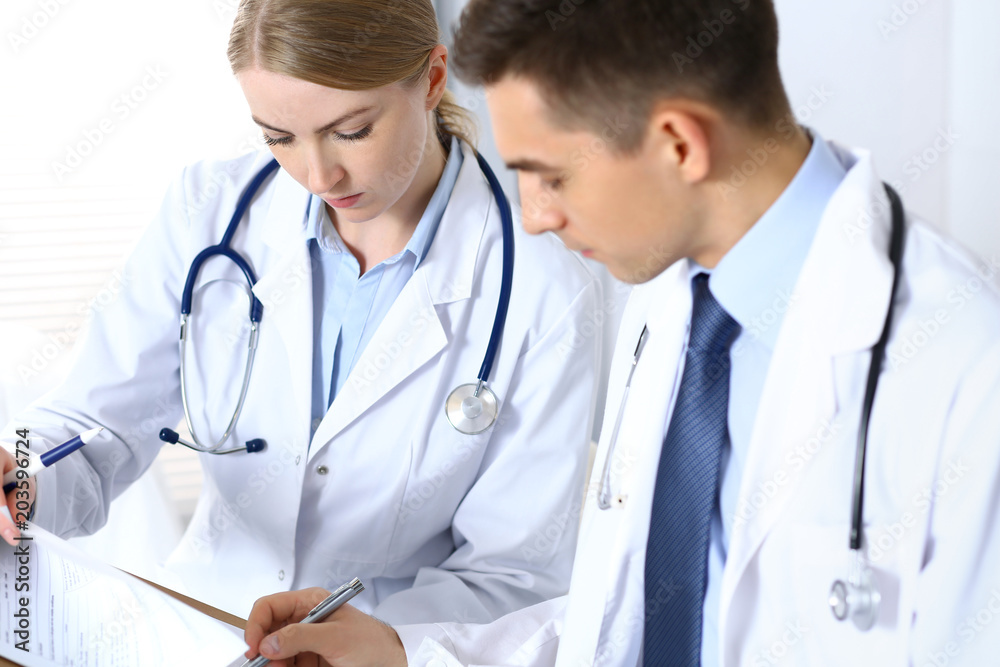 Doctors writing papers using clipboard. Physicians discussing medication program or studying at medical conference. Healthcare, insurance and medicine concept Doctors writing papers using clipboard. Physicians discussing medication program or studying at medical conference. Healthcare, insurance and medicine concept
