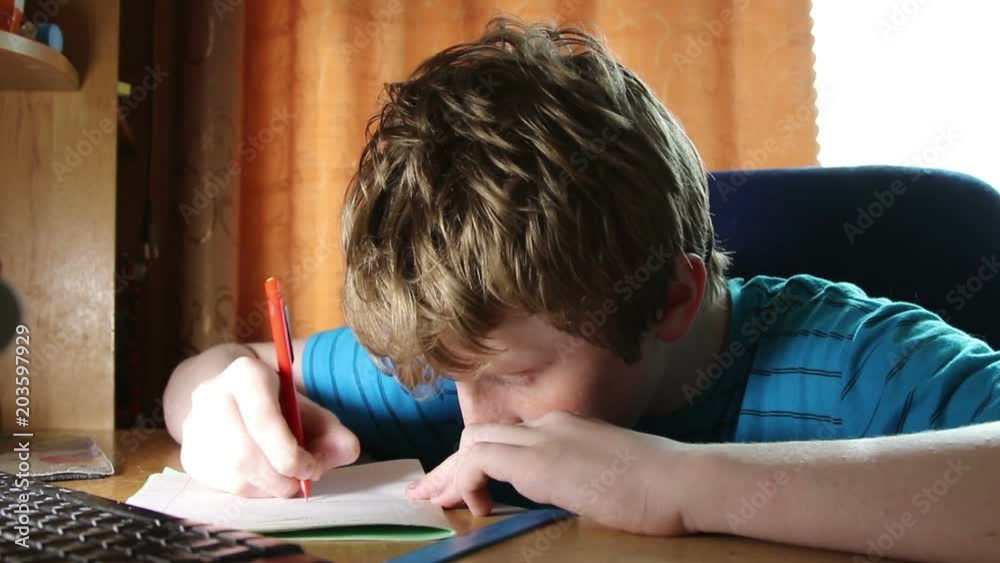 The boy writes in a notebook. A child is doing a school assignment at home.
The boy writes in a notebook. A child is doing a school assignment at home.