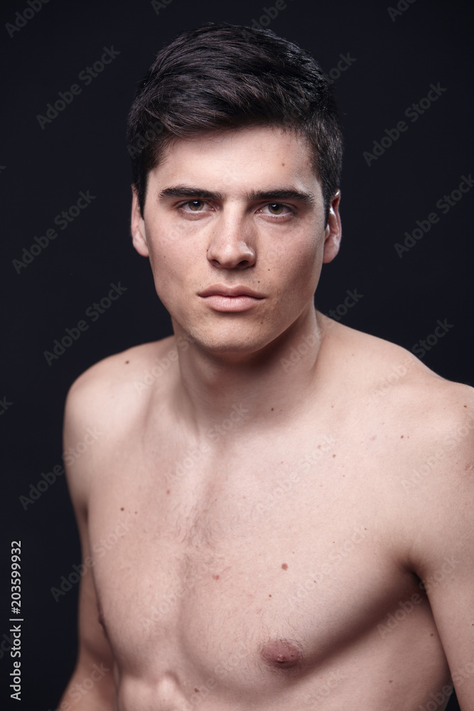 one young handsome man, model shirtless, simple studio upper body shot, black background.