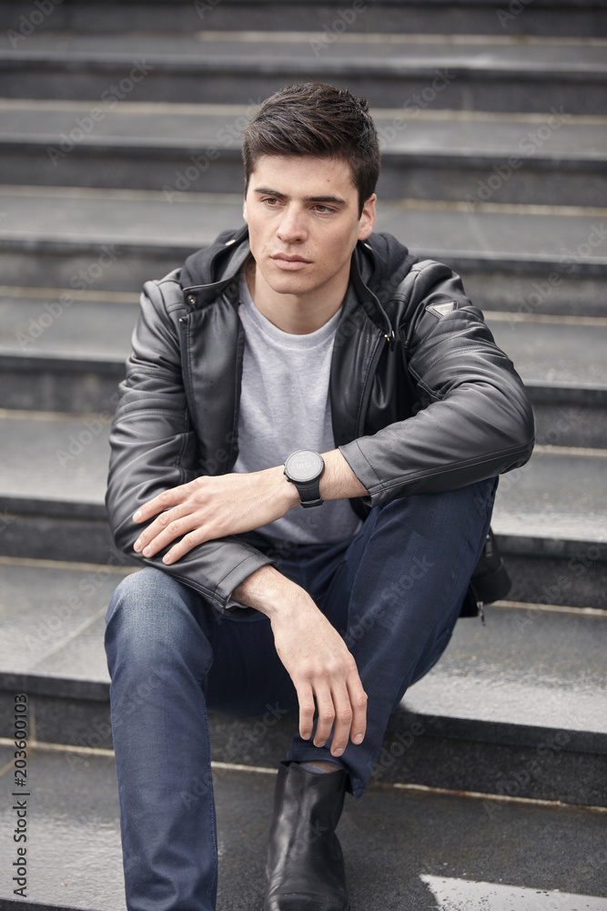 handsome man sitting on steps, wearing casual clothes. overcast autumn day.