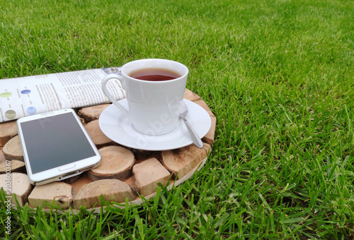 Cup of coffee or tea on a wooden tray on a grass with smartfone and newspaper photo