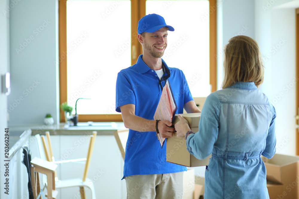 Smiling delivery man in blue uniform delivering parcel box to recipient - courier service concept. Smiling delivery man in blue uniform Smiling delivery man in blue uniform delivering parcel box to recipient - courier service concept. Smiling delivery man in blue uniform