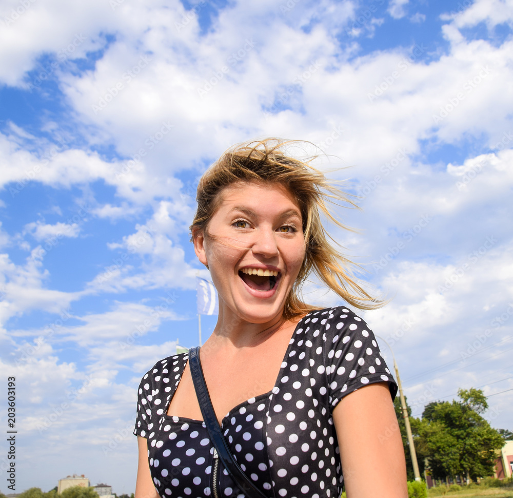 Laughing blond girl against the sky with clouds.