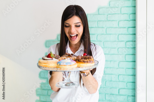 Beautiful young woman enjoying in delicious glazed and decorated donuts. 