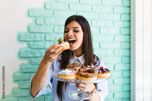 Beautiful young woman enjoying in delicious glazed and decorated donuts. 