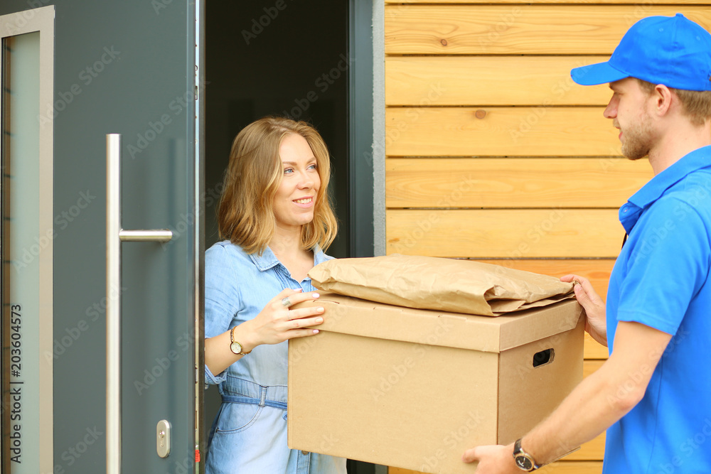 Smiling delivery man in blue uniform delivering parcel box to recipient - courier service concept. Smiling delivery man in blue uniform Smiling delivery man in blue uniform delivering parcel box to recipient - courier service concept. Smiling delivery man in blue uniform