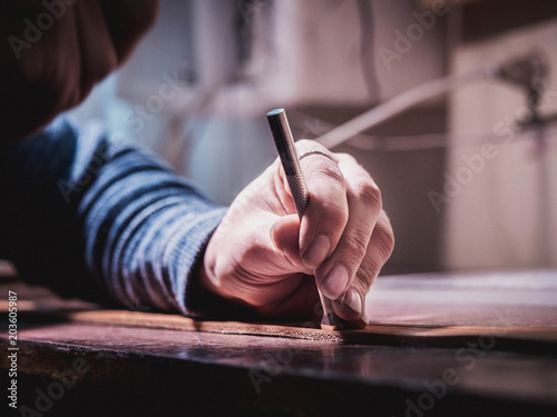Close up of leather craftsman working with natural leather using hammer. Handbag master at work in local workshop. Handmade concept. Male shoemaker creating product with textile