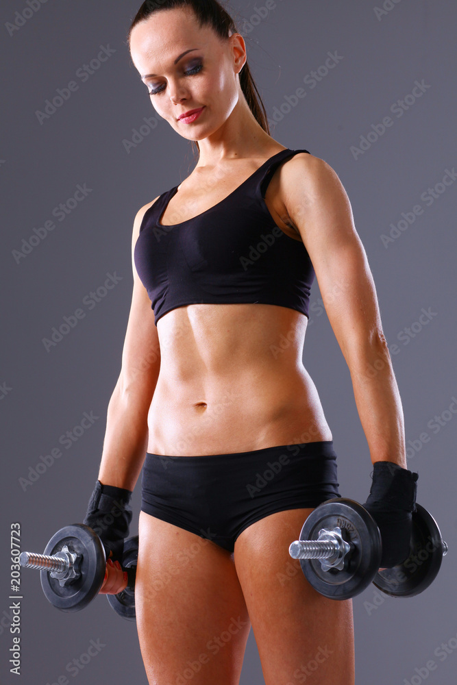Muscular young woman standing on gray background. Muscular young woman Muscular young woman standing on gray background. Muscular young woman